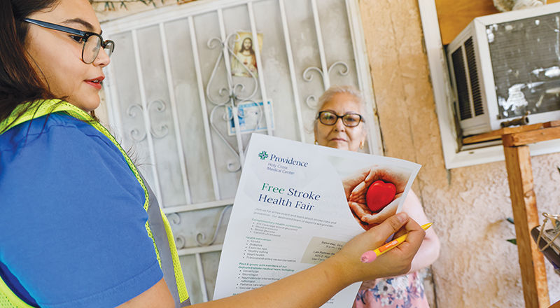 Scarlett Diaz, a Providence St. Joseph Health community health worker, talks to Lucia Flores on the porch of Flores’ home in San Fernando, California.